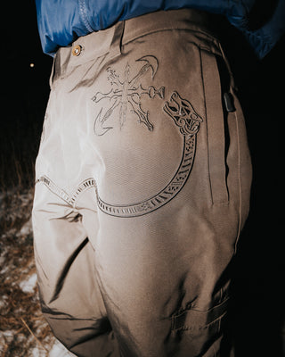 Brown pants with intricate designs worn by a person in a dark setting