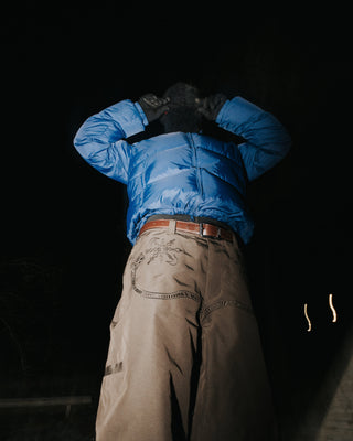 Person wearing a blue jacket and brown pants against a dark background