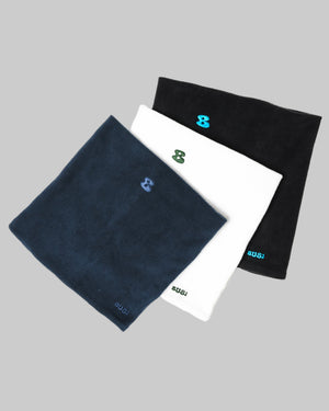 Three neckwarmers laid out on a white background, one dark blue, one white with a pattern, and one black with a pattern.