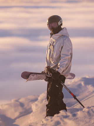 Person in winter gear holding a snowboard and ski pole on a snowy landscape