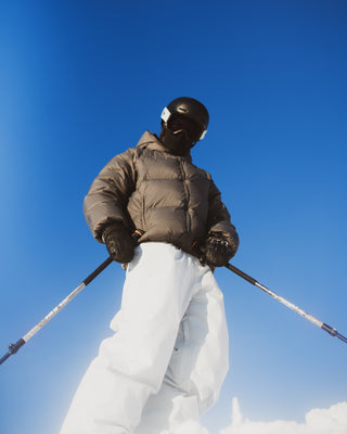 Person in winter gear with skis and poles against a clear blue sky