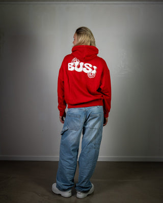 Person wearing a red hoodie with 'BUSI' logo on the back, standing against a plain wall.